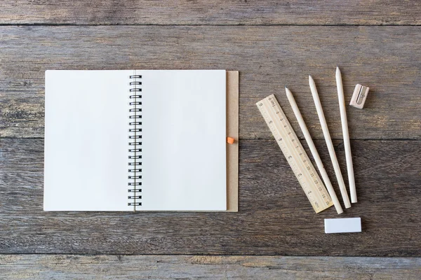 Open notebook on wooden background with pencils and ruler.