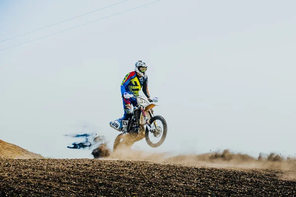 Racer on a motorcycle rides on rear wheel on a dusty track