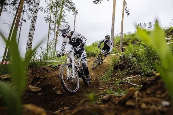 Two riders of athlete on bike down through woods from mountain