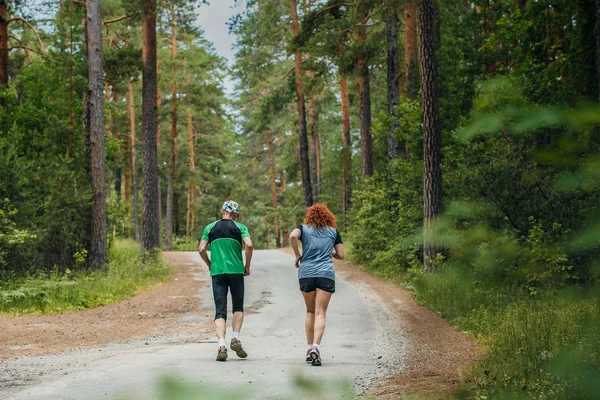 Man and woman running along road in forest