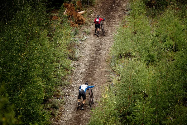 Two athlete mountainbiker walking with bicycle uphill