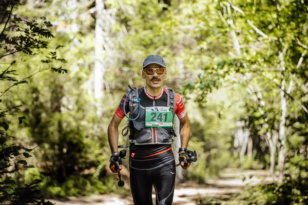 Male athlete midlife age runs in woods with nordic poles in hand