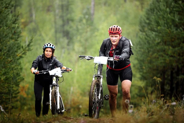 Pair of male and female mountainbikers climb a step uphill in forest