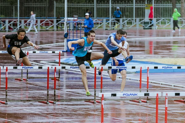 Young athletes run 110 meter hurdles  in the rain