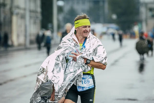 Athlete runner middle-aged after the finish put on aluminum foil