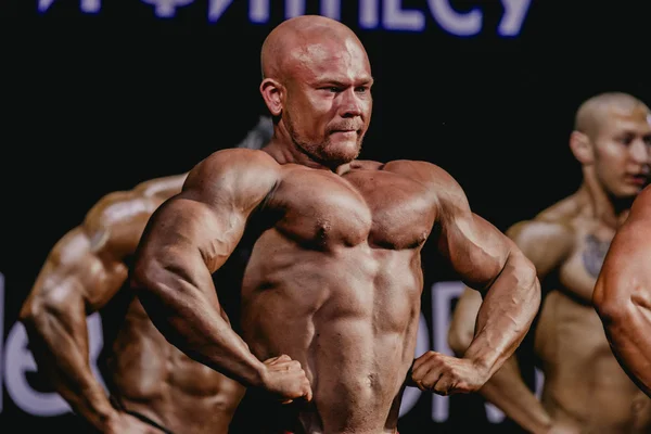 Athlete bodybuilder in a pose facing forward, straining chest and press