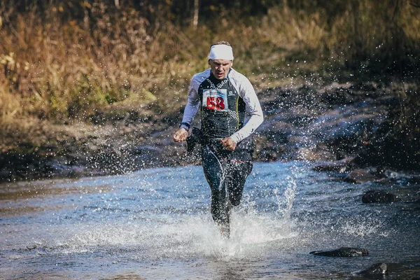 Runner middle-aged man crossing river, and around him water splashes