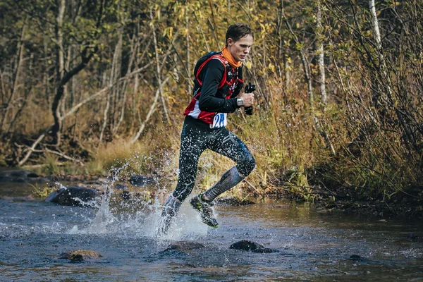 Young man runner splash water in river, during crossing a mountain river