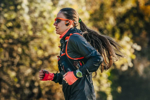 Young woman athlete with watch and headphones running through woods