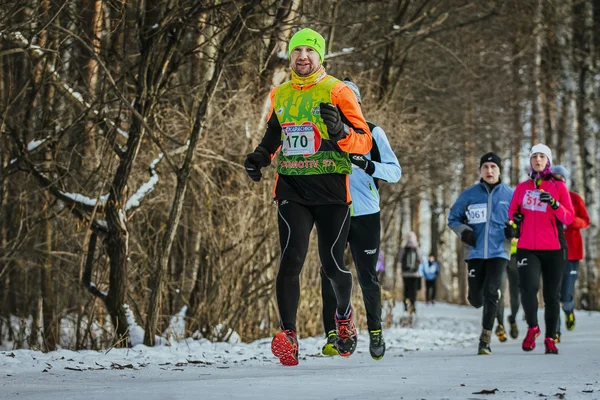 Happy young athlete man running in front group of athletes in winter woods