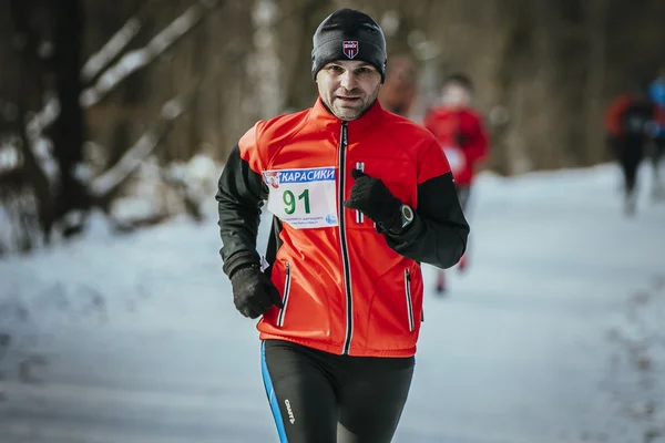 Man middle-aged runner runs through snowy Park alley in December