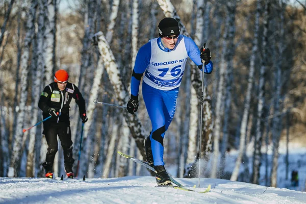 Rivalry men skiers race classic style in a birch forest in winter