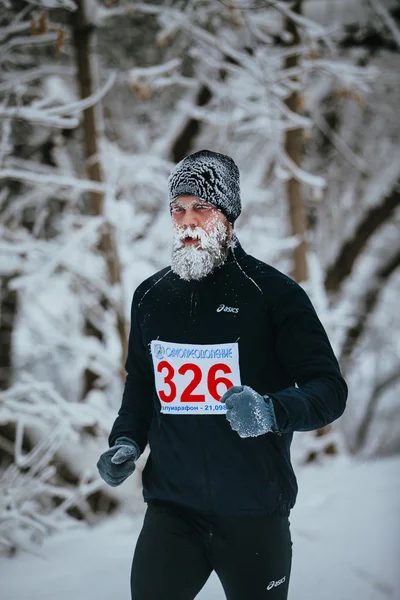 Young male jogger running through a snowy Park alley. face and beard in frost