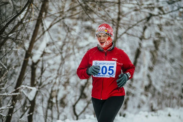 Middle-aged woman athlete running on winter snow-covered alley in Park