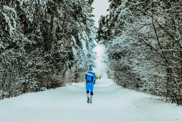 Man in sportswear running through alley in winter forest