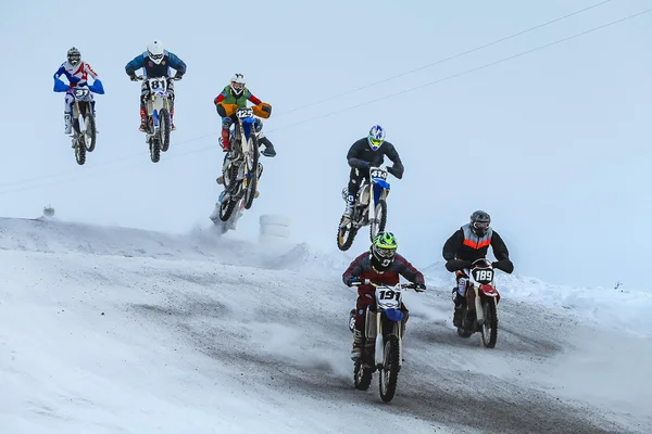 Group motorcycle racer riding on snow-covered mountain after start