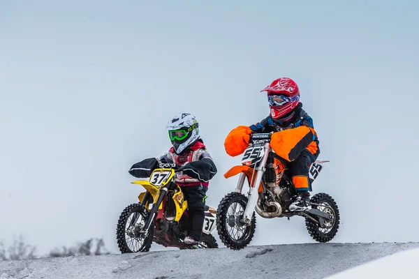 Two young boy racers on motorcycle ride through hill of motocross