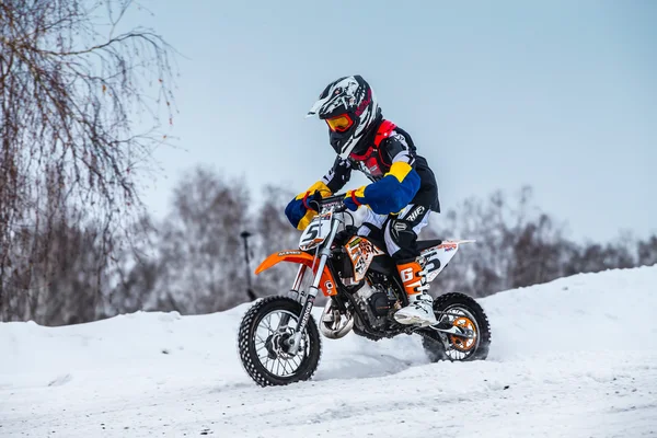Closeup little boy racers motorcycle rides through snow-covered motocross track