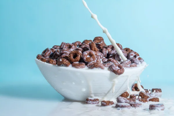 Milk stream jet pouring into a cup with chocolate flakes in the form of rings, splashes of milk on a light blue background