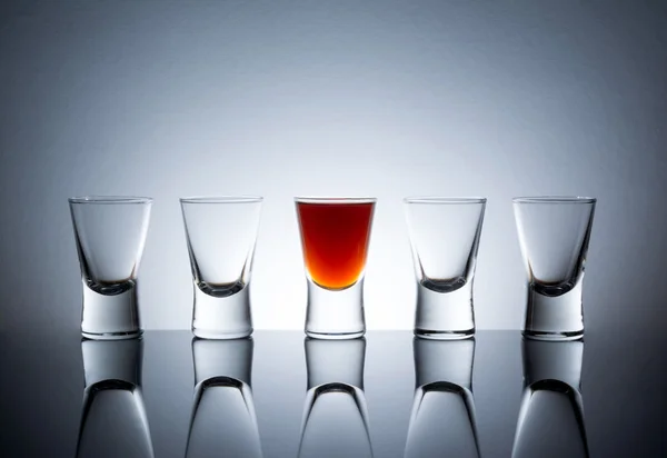 One full shot glass with alcohol drink with reflection next to the empty glasses, Full glass near empty glasses
