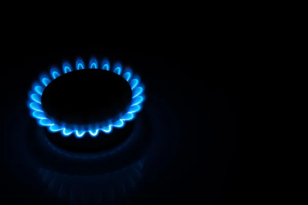 Burning gas stove hob blue flames close up in the dark on a black