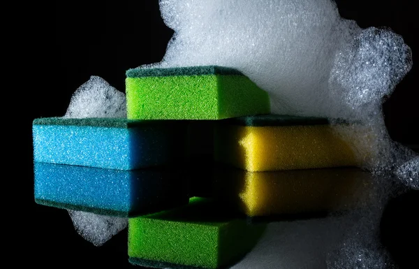 Colorful sponges with foam and reflection, bubbles, isolated on black background