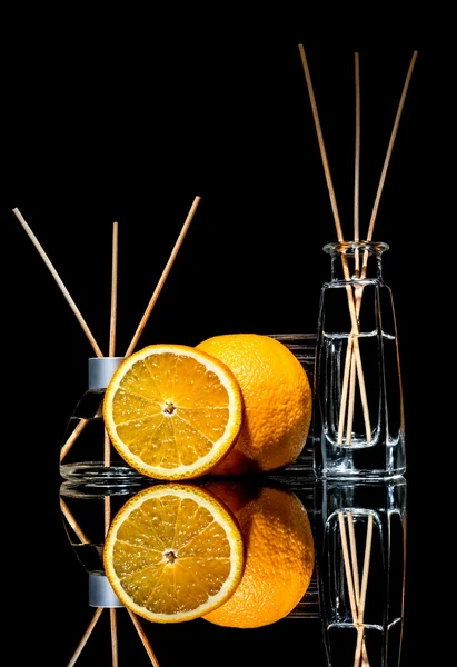 Air fresheners with orange fruits scent in a beautiful glass jars with sticks and whole orange and a slice of orange with reflection isolated on a black