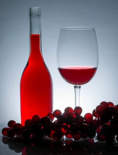 Wine in a glass next to a bottle of wine and grapes on a table with reflection on a vintage background