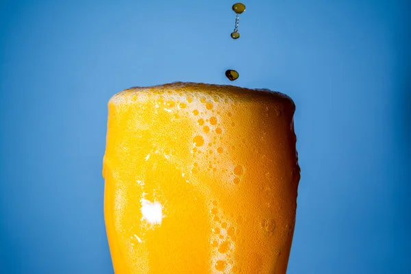 Orange soda large glass, overflowing glass of orange soda closeup with bubbles on blue background