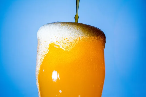Orange soda large glass, overflowing glass of orange soda closeup with bubbles on blue background