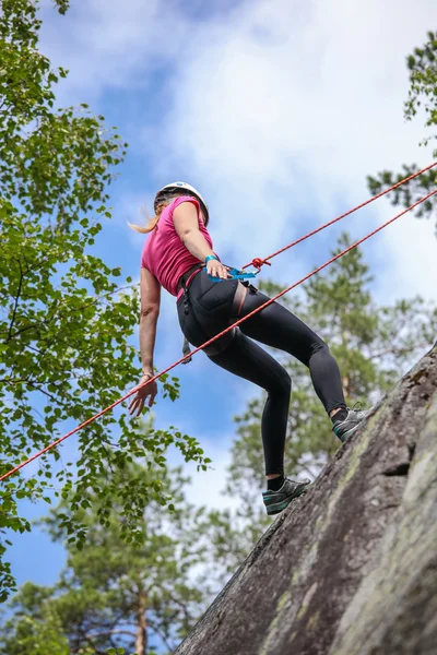 Young woman practicing climbing on natural rocks