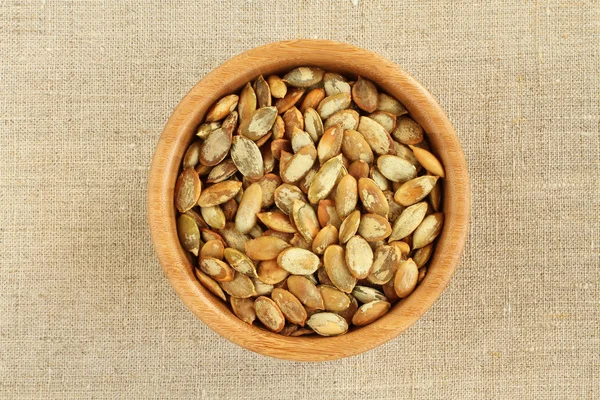 Shelled  roasted pumpkin seeds in bamboo bowl on rough linen cloth