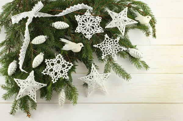 Christmas decoration - white cotton crocheted stars, snowflakes, whitebirds and silver cones on green spruce branches on white wooden background