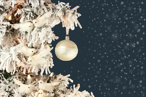 Decoration on Christmas tree - white birds and silver ball on snowy spruce on blue background with snow mist