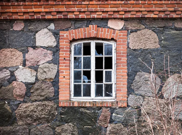 Window with broken glass in the wall of the house made of natural stone and red brick