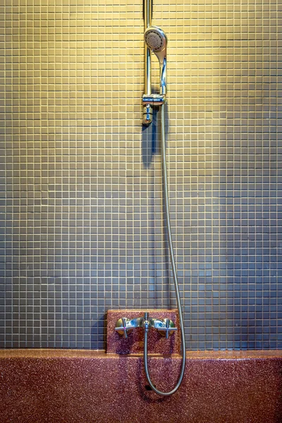 Shower head on ceramic tile wall with empty red bathtub