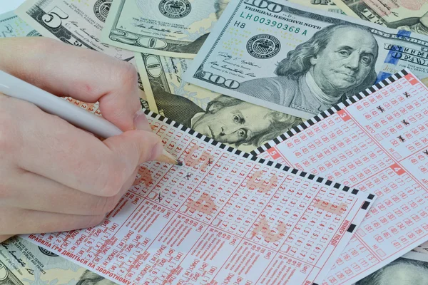 The hand is writting on lottery ticket on dollar background
