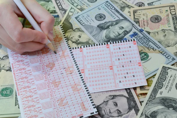 The hand is writting on lottery ticket on dollar background