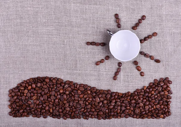 Composition cup of coffee with sun and sea made by coffee beans on linen texture table