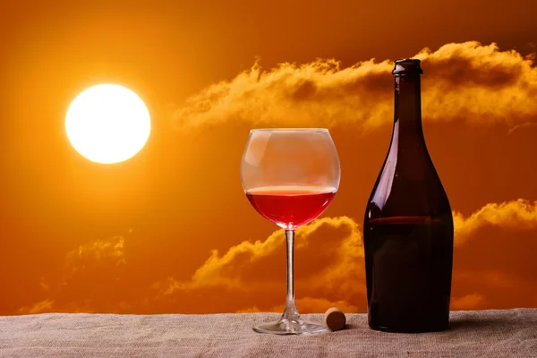 Bottle and glass of red wine on the linen table against the colorful landscape sunset moon