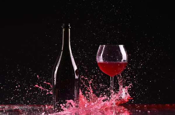 Bottle and glass with red wine, red wine splash, wine pouring on table on dark black background, big splash around Glass and bottle of red wine splash on black