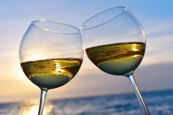 Romantic glass of wine sitting on the beach at colorful sunset Glasses of white wine against sunset, white wine on the sky background with clouds