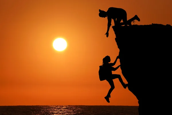 The joint work teamwork of two people man and girl travelers help each other on top of a mountain climbing team, a beautiful sunset landscape.