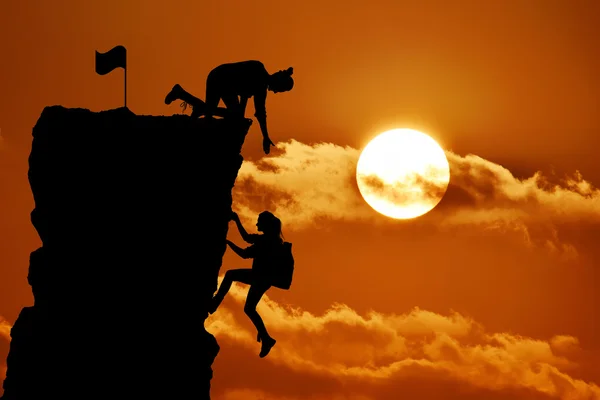 The joint work teamwork of two people man and girl travelers help each other on top of a mountain climbing team, a beautiful sunset landscape.