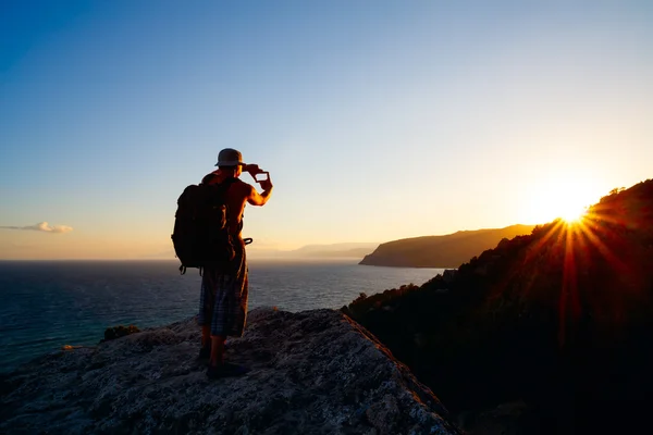 Landscape photographer traveler man on cliff above the sea in summer rays of setting sun is studying  compositional structure of frame