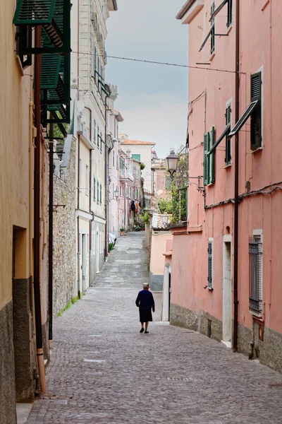 A old woman walking alone in a narrow street of a small village