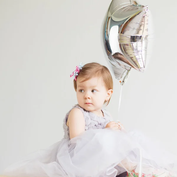 Little baby girl holding silver star-shaped balloon.