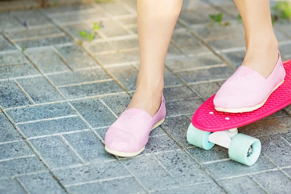 Girl standing on a pink skateboard outdoors. Closeup image of fe