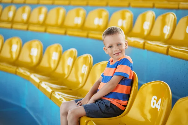 Little boy sitting in an empty stadium among yellow plastic numb