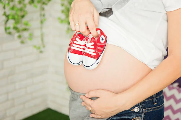 Pregnant woman holding baby shoes on her belly